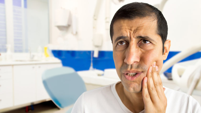 Man in a dental chair holding his cheek with tooth pain