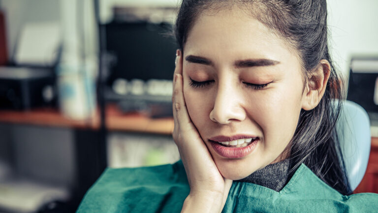 Woman in a dental chair holding her cheek in pain