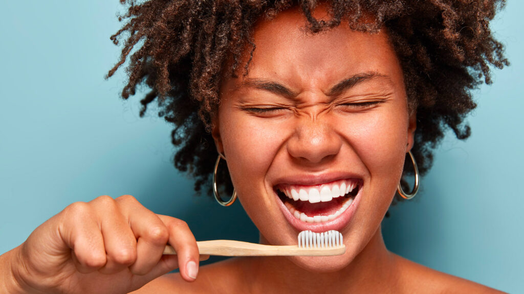 Young female smiling with her eyes closed holding a toothbrush up to her mouth after having teeth whitening treatment.