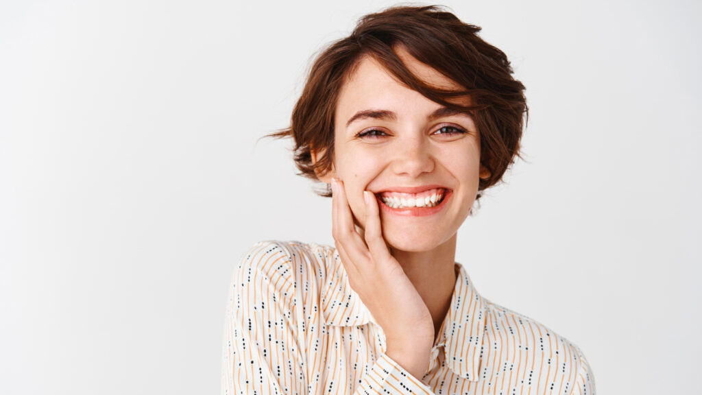 Young girl smiling with her hand on her face, happy because she just left her teeth whitening appointment.